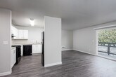 This single-floor residence offers a clean, functional layout designed for comfortable everyday living. The interior is finished with warm, neutral tones and consistent wood-style plank flooring running through the main living areas, complemented by plush carpeting in both bedrooms.

The kitchen is a standout feature, offering ample cabinetry with white shaker-style cabinets, light countertops, and a full suite of black appliances including an electric range, dishwasher, and refrigerator. A peninsula-style pass-through connects the kitchen to the main living area, enhancing the open feel of the space.

The living room is generously sized, bathed in natural light from a large sliding glass door that opens to a private balcony overlooking lush greenery. A ceiling fan adds both comfort and practicality to the space.

Both bedrooms are well-proportioned, featuring neutral carpet, windows that bring in natural light, and ample wall space for furniture arrangement. A hallway connects the bedrooms to the full bathroom, which includes a single-sink vanity with a light countertop, a tub-shower combination, and clean white fixtures throughout.

A sliding closet and additional doors along the hallway provide convenient storage options. A smoke detector is ceiling-mounted in the hall, reflecting practical safety considerations. The overall design is cohesive, clean, and move-in ready.