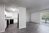 This single-floor residence offers a clean, functional layout designed for comfortable everyday living. The interior is finished with warm, neutral tones and consistent wood-style plank flooring running through the main living areas, complemented by plush carpeting in both bedrooms.

The kitchen is a standout feature, offering ample cabinetry with white shaker-style cabinets, light countertops, and a full suite of black appliances including an electric range, dishwasher, and refrigerator. A peninsula-style pass-through connects the kitchen to the main living area, enhancing the open feel of the space.

The living room is generously sized, bathed in natural light from a large sliding glass door that opens to a private balcony overlooking lush greenery. A ceiling fan adds both comfort and practicality to the space.

Both bedrooms are well-proportioned, featuring neutral carpet, windows that bring in natural light, and ample wall space for furniture arrangement. A hallway connects the bedrooms to the full bathroom, which includes a single-sink vanity with a light countertop, a tub-shower combination, and clean white fixtures throughout.

A sliding closet and additional doors along the hallway provide convenient storage options. A smoke detector is ceiling-mounted in the hall, reflecting practical safety considerations. The overall design is cohesive, clean, and move-in ready.