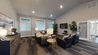 Located in Portland, Oregon, the Lakemont Ridge leasing office is a single-story community space thoughtfully designed to welcome residents and visitors alike. Guests are greeted at the entrance by a striking reception desk crafted from natural driftwood with a glass top, set against a wall bearing the Lakemont Ridge name in sleek metallic lettering. Light wood flooring extends through the entryway, where a live-edge wood bench and framed property displays line the walls alongside glass-paned double doors that invite generous natural light inside.

The main lounge area is expansive and open, featuring vaulted ceilings with recessed lighting and large windows fitted with white blinds that frame views of surrounding greenery. Richly patterned, multi-tone carpet tiles ground the space and add visual texture. Multiple seating arrangements with leather sofas, tufted chairs, and accent tables create distinct conversation areas, complemented by lush potted plants and wall-mounted televisions. A sideboard with a coffee station anchors one side of the room.

A dedicated workstation area off the entrance provides a rustic wood high-top table with ergonomic seating beneath bright, window-lit walls—ideal for meetings or quick tasks. The overall ambiance balances contemporary design with warm, natural materials, projecting a professional yet comfortable atmosphere throughout.