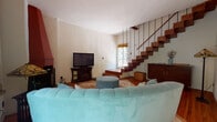 This two-story home combines rustic character with classic elegance across a well-appointed layout. The main living area serves as the heart of the home, centered around a distinctive terracotta corner fireplace that rises dramatically toward the ceiling. Warm hardwood floors run throughout, and a floating open-riser staircase with slender rod railings connects the two levels, adding an architectural focal point to the space. Natural light filters in through large windows, offering views of lush outdoor greenery.

The kitchen is well-equipped, featuring crisp white cabinetry paired with striking dark granite countertops, stainless steel appliances, and warm hardwood flooring. Sheer curtained windows brighten the workspace with natural light.

The dining area is intimate and refined, appointed with a round wooden table beneath an ornate crystal chandelier, and framed by French doors that open to a verdant garden setting.

Upstairs, the bedrooms showcase soaring vaulted ceilings with exposed wooden beam and brick detailing, lending a warm, rustic ambiance. The primary bedroom includes an en-suite bathroom and generous natural light through large windows.

The bathroom features classic white subway tiling accented by decorative cobalt and patterned tiles, terracotta floor tiles, and a pedestal sink, completing the home's eclectic and characterful aesthetic.
