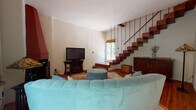 This two-story home combines rustic character with classic elegance across a well-appointed layout. The main living area serves as the heart of the home, centered around a distinctive terracotta corner fireplace that rises dramatically toward the ceiling. Warm hardwood floors run throughout, and a floating open-riser staircase with slender rod railings connects the two levels, adding an architectural focal point to the space. Natural light filters in through large windows, offering views of lush outdoor greenery.

The kitchen is well-equipped, featuring crisp white cabinetry paired with striking dark granite countertops, stainless steel appliances, and warm hardwood flooring. Sheer curtained windows brighten the workspace with natural light.

The dining area is intimate and refined, appointed with a round wooden table beneath an ornate crystal chandelier, and framed by French doors that open to a verdant garden setting.

Upstairs, the bedrooms showcase soaring vaulted ceilings with exposed wooden beam and brick detailing, lending a warm, rustic ambiance. The primary bedroom includes an en-suite bathroom and generous natural light through large windows.

The bathroom features classic white subway tiling accented by decorative cobalt and patterned tiles, terracotta floor tiles, and a pedestal sink, completing the home's eclectic and characterful aesthetic.