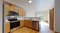 This single-floor residence offers a thoughtfully designed layout that balances function and comfort throughout its key living spaces. The kitchen is a standout feature, showcasing warm honey-toned wood cabinetry, light-colored countertops, and a full suite of stainless steel appliances including a refrigerator, electric range with over-the-range microwave, and dishwasher. Light hardwood flooring runs throughout the kitchen and living areas, adding warmth and continuity. A peninsula with a breakfast bar creates a natural division between the kitchen and the adjacent living space, which benefits from a sliding glass door that draws in generous natural light and provides outdoor access. The open sightlines between the kitchen and living area make the space feel connected and airy. The bedroom is carpeted for comfort and features a closet with a rod and shelving system, offering practical storage. Natural light filters into the bedroom, creating a calm and restful atmosphere. The bathroom is clean and functional, featuring a full soaking tub with a shower surround finished in crisp white. Throughout the space, interior doors are finished in light wood tones that complement the overall palette of neutral walls and warm flooring, resulting in a cohesive and inviting living environment.