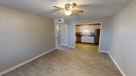 This single-floor unit is organized around an open-concept layout that connects the living area directly to the kitchen, creating a cohesive and functional living space. Throughout the main areas, light wood-look flooring adds a clean, contemporary feel, while neutral gray walls provide a versatile backdrop. Ceiling fans with integrated lighting fixtures are installed in the living areas, supporting both air circulation and ambient lighting.

The kitchen is well-equipped with abundant white cabinetry offering generous storage above and below the counter. Dark laminate countertops contrast neatly with the white cabinets, and the space includes a stainless steel refrigerator, a stainless steel dishwasher, and a stainless steel range. A double-basin sink is centrally positioned beneath upper cabinets. The textured popcorn ceiling is consistent throughout the unit.

The bedrooms feature soft gray carpeting and receive natural light through windows fitted with blinds. Closet space is provided with built-in rods and shelving. The bathroom includes a full-size soaking tub with a shower fixture and chrome hardware, finished in a clean white surround. A louvered closet door near the living area provides additional storage. The overall ambiance is neutral, clean, and move-in ready.