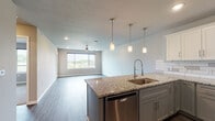 Located in Springfield, MO, this single-floor residence offers a thoughtfully designed open-concept layout that seamlessly connects the kitchen, dining, and living areas. The kitchen is a standout feature, showcasing granite countertops, a central island with a stainless steel undermount sink and pendant lighting above, and a full suite of stainless steel appliances including a refrigerator with ice maker, electric range, over-the-range microwave, and dishwasher. Two-toned cabinetry — white uppers paired with sage-gray lowers — is complemented by a classic white subway tile backsplash, adding a clean, contemporary aesthetic. Wood-style luxury vinyl plank flooring extends throughout the main living areas, providing both durability and visual continuity. The spacious living area benefits from natural light through a large sliding window with outdoor views of the surrounding landscape, and a ceiling fan overhead. The bedroom features plush carpet, a ceiling fan, and its own large window with scenic views. The bathroom is well-appointed with a granite-topped vanity, shaker-style cabinetry, a large mirror, and a full tub-shower combination. Recessed lighting throughout the unit enhances the bright, modern ambiance of this well-finished space.