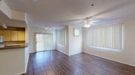 This single-story residence offers a well-organized layout designed for comfortable everyday living. The living area is a standout feature, showcasing rich wood-style flooring, a ceiling fan with light fixture, and multiple large windows dressed with vertical blinds that allow generous natural light to fill the space. A sliding glass door provides direct access to the outdoors, further enhancing the bright, open feel. Track lighting adds a layer of practicality and style to the living zone.

The kitchen is efficiently laid out in a U-shape configuration, equipped with light-toned cabinetry, laminate countertops, a double-basin stainless steel sink, and white appliances including an electric range, built-in microwave, and dishwasher. Track lighting overhead ensures the workspace is well-illuminated.

The bedrooms are carpeted for warmth and comfort, each featuring ceiling fans, vertical blind-covered windows for natural light, and dedicated closet space. One bedroom includes a walk-in closet, while another is served by a sliding-door closet with built-in rods for organized storage. The neutral wall tones and consistent design elements throughout the unit create a cohesive, clean aesthetic that is both functional and inviting.