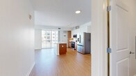 Located at 1657 Fairport Nine Mile Point Road in Penfield, NY, this single-floor, one-bedroom, one-bathroom unit offers a well-designed layout that maximizes its comfortable footprint. The open-concept kitchen and living area serves as the heart of the space, featuring light wood-style flooring that flows throughout. The kitchen is appointed with stainless steel appliances — including a French door refrigerator, electric range, and microwave — complemented by a two-tone cabinetry design of warm wood lower cabinets and crisp white upper cabinets. A central island with a white quartz countertop and integrated sink provides additional prep space and casual dining potential. Track lighting overhead adds a modern touch. The bedroom is a well-proportioned retreat finished with plush carpeting and two windows that frame peaceful views of lush greenery. A generously sized walk-in closet with wire shelving provides excellent storage. The bathroom is clean and contemporary, showcasing a warm wood vanity with white countertop, an undermount sink, modern fixtures, a large mirror, and a shower with grab bars. A dedicated utility room and hallway round out this thoughtfully organized, move-in-ready space.