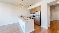 Located at 1525 14th Ave in Seattle's Capitol Hill neighborhood, this one-bedroom unit offers a well-designed single-floor layout making efficient use of its space. Warm hardwood flooring flows throughout the main living areas and hallways, lending a cohesive and inviting feel across the unit.

The open-concept kitchen and living room serve as the heart of the home. The kitchen is equipped with stainless steel appliances — including a refrigerator, range, and microwave — complemented by dark wood cabinetry, light quartz countertops, and a peninsula island with an undermount sink and pendant lighting above. Track lighting adds a modern touch, while large floor-to-ceiling windows and a sliding glass door flood the living area with abundant natural light and offer views of the surrounding Seattle cityscape.

The bedroom continues the hardwood flooring and features expansive windows on two walls, maximizing light and outdoor views. Two closets provide ample storage throughout the unit. The bathroom includes a full soaking tub and shower combination, a dark wood vanity with a light countertop, a large mirror, and tile flooring, with an adjacent shelved linen closet for added organization. An in-unit laundry area adds everyday convenience, completing this thoughtfully appointed urban residence.