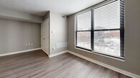 Located at 722 Walnut St in Kansas City, MO, this 2-bedroom, 1-bathroom unit offers a practical and well-appointed layout across a single floor. The entrance opens directly adjacent to the kitchen, which is equipped with rich dark wood cabinetry, a tile backsplash, light countertops, and black appliances including a refrigerator, dishwasher, electric range, and microwave. Hardwood-style flooring runs throughout the entire unit, lending a cohesive and modern feel to every room. The living room is open and bright, benefiting from natural light through large windows that offer views of the surrounding Kansas City cityscape. Both bedrooms are comfortably sized, featuring neutral gray walls, ample natural light through blinded windows, and dedicated closet space. The primary bedroom is generously proportioned and includes a built-in closet. The full bathroom features a tiled tub-shower surround with warm earth-toned stone tile and a standard white soaking tub. A hallway connects the main living areas to the bedrooms and bathroom, with additional closets providing practical storage. A utility room and three closets throughout the unit further enhance functionality. The overall ambiance is clean, contemporary, and move-in ready.