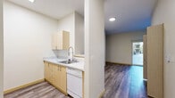 Located in Seattle's Greenwood neighborhood, this one-bedroom, one-bathroom unit offers a well-designed layout that maximizes its compact footprint. The combined kitchen and living area forms the heart of the space, featuring durable hardwood-style flooring throughout. The kitchen is outfitted with light wood cabinetry, light-toned countertops, a stainless steel sink with a pull-down faucet, and a dishwasher, all neatly arranged along one wall. Recessed and flush-mount ceiling lighting keeps the area bright and functional. The adjacent living area is open and versatile, with a clean, neutral palette of white walls and warm wood baseboards. A pass-through view into the kitchen adds a sense of connectivity between the two spaces. The bedroom is carpeted for comfort and features a sliding glass door that opens directly to an outdoor area, allowing natural light and green views to fill the room. A built-in closet with sliding doors provides convenient storage. The bathroom includes a full tub-shower combination with a curved curtain rod, neutral surround tiles, and wood-style flooring that ties cohesively to the rest of the unit. A dedicated closet off the main hallway adds further storage capacity. The overall design is clean, modern, and practical.