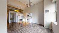 This thoughtfully laid-out one-bedroom, one-bathroom unit offers a compelling mix of modern design and functional living. The open-concept living and kitchen area is immediately striking, defined by dramatically high ceilings fitted with a ceiling fan and industrial-style track lighting. Rich, wide-plank hardwood floors extend throughout the main living space, complementing the clean, contemporary aesthetic.

The kitchen is well-appointed with white cabinetry — including glass-front upper cabinets and a decorative X-pattern wine rack — granite countertops, white appliances, a tile backsplash, and a deep sink. A freestanding granite-topped kitchen island on casters provides additional workspace and flexibility. Windows in the living area invite natural light and offer views of the surrounding cityscape.

The bedroom features soft carpet flooring and a raised ceiling detail, contributing to a calm and private atmosphere. A mirrored sliding door opens to a dedicated walk-in closet with built-in wire shelving, offering generous storage.

The bathroom is finished with large-format geometric tile flooring in a diagonal pattern, a soaking tub, a handheld shower with subway tile surround, and clean white fixtures throughout — creating a bright, spa-like feel. This unit balances urban-modern design with practical, comfortable living.