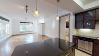 This single-floor residence is designed with a clean, contemporary aesthetic that balances functionality and style throughout its open layout. The living area is anchored by gleaming hardwood floors that reflect natural light pouring in through two large windows overlooking lush greenery. Track lighting runs along the ceiling, complementing the bright, white walls to create an airy, well-lit atmosphere.

The kitchen is a standout feature, outfitted with rich dark-wood cabinetry, dark granite countertops, and a classic subway tile backsplash. A tray ceiling adds architectural detail overhead, while stainless steel appliances — including a dishwasher, wall oven, microwave, and refrigerator — provide a polished, modern finish. A kitchen island with matching dark granite extends the prep space and opens seamlessly toward the living area via dual pendant lights.

A sliding door leads to a well-appointed full bathroom featuring light travertine tile flooring, dark wood vanity cabinetry, a soaking tub, and a separate glass-enclosed shower. Directly accessible from the bathroom is a spacious walk-in closet with built-in shelving and hanging rods on multiple walls.

A dedicated laundry room with side-by-side washer and dryer and additional shelving rounds out this thoughtfully designed space.