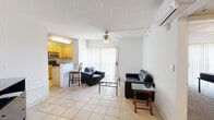 This well-organized 1-bedroom, 1-bathroom unit offers an efficient single-floor layout designed to maximize every square foot. The open-concept living area features light-toned ceramic tile flooring, a ceiling fan, and a wall-mounted air conditioning unit, with a sliding glass door fitted with vertical blinds that fills the space with natural light. The kitchen is well-appointed with warm wood cabinetry, granite-style countertops, stainless steel appliances including an over-the-range microwave and electric range, and a breakfast bar that provides additional seating and a natural transition from the kitchen to the living area. The bedroom is a comfortable retreat with carpeted flooring, a ceiling fan, and its own sliding glass door with vertical blinds offering natural light and outdoor views. Two closets provide ample storage throughout the unit. The bathroom is neatly finished with tile flooring, a granite-topped wood vanity, a large mirror, and a full-size soaking tub with a shower. The textured ceilings throughout contribute to the unit's consistent and practical aesthetic, making this a highly functional living space.