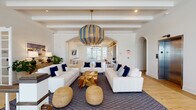 Located at 898 Water Tower Way in Lantana, Florida, this coastal-inspired clubhouse offers a thoughtfully designed single-floor amenity space that blends relaxed elegance with resort-style functionality. The interiors are unified by a crisp white-and-navy color palette, warm hardwood flooring, and an abundance of natural light throughout.

The expansive main lounge serves as the heart of the space, featuring exposed beam ceilings, graceful archways, and a striking blue-and-natural-fiber pendant light. White sofas, navy accent pillows, woven ottomans, and a driftwood coffee table lend a relaxed, nautical character. A secondary sitting room offers tray ceilings with subtle ambient lighting, rattan armchairs, and wall-mounted TV for a more intimate gathering experience.

The kitchen and dining area features a large white island with bar seating, pendant lighting, a patterned tile backsplash, open shelving, and a built-in dining nook with navy accents. The game room is a standout, housing both a pool table and a shuffleboard table beneath dramatic wagon-wheel chandeliers, with French doors opening to outdoor views. Built-in shelving with woven baskets and shiplap wall detailing add warmth. A dedicated golf simulator room with turf flooring and projection screen rounds out the entertainment offerings. A carpeted lounge area with sweeping windows and navy blue furnishings provides a bright, comfortable retreat.