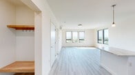 Located at 70 Cambrian Way in Burlington, Vermont, this thoughtfully designed one-bedroom, one-bathroom residence offers a bright and efficient single-floor layout. The open-concept living and kitchen area is bathed in natural light from an expansive bank of large windows that frame picturesque outdoor views, creating an airy and welcoming atmosphere throughout. Light-toned hardwood-style flooring flows seamlessly through the main living spaces, complementing the clean white walls and modern finishes.

The kitchen is well-appointed with crisp white shaker cabinetry, stone-look countertops, a kitchen island with pendant lighting, and a full suite of stainless steel appliances including a refrigerator, range, microwave, and dishwasher. A wall-mounted mini-split system provides efficient climate control in the living area.

The bedroom is a comfortable retreat with plush carpeting, multiple windows offering natural light and outdoor views, and direct access to a dedicated closet fitted with wire shelving and hanging rods. The bathroom features light tile flooring, white cabinetry with stone countertops, and a clean, neutral palette. An entry hallway with built-in coat hooks and wood shelving adds practical functionality upon arrival, completing this well-organized and modern Burlington residence.