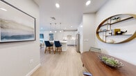 This thoughtfully designed single-floor residence offers a seamless open-concept layout that connects the kitchen, dining, and living areas into one cohesive, light-filled space. Light wood-look flooring runs throughout the main living areas, complementing the crisp white walls and recessed lighting overhead.

The kitchen is a standout feature, showcasing white shaker-style cabinetry extending to the ceiling, a large center island with a quartz countertop and seating for two, stainless steel appliances including a refrigerator, range, and microwave, and a classic subway tile backsplash. Pendant lights suspended above the island provide both task lighting and a modern aesthetic touch.

The living room offers a relaxed, comfortable atmosphere with soft sage-green walls, light hardwood-style flooring, and a sliding glass door that opens to a private balcony, allowing for an abundance of natural light and outdoor access.

The bedroom is a calm retreat, featuring plush carpeting, soft neutral wall tones, and windows that bring in natural daylight. The bathroom is finished with marble-look tile flooring, white cabinetry, and a well-lit vanity mirror, offering a clean and polished feel. A stacked in-unit washer and dryer adds everyday convenience to this well-rounded residence.