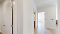 This single-floor residence offers a clean, contemporary design characterized by crisp white walls, light hardwood flooring, and an abundance of natural light throughout. The open-concept living room is generously proportioned, featuring multiple large windows that frame outdoor views of the surrounding neighborhood and mature trees, flooding the space with sunlight.

The kitchen is thoughtfully designed with warm wood-toned cabinetry extending from floor to ceiling, light quartz countertops, a double stainless steel sink, and a full suite of stainless steel appliances including a range, built-in microwave, and dishwasher. A clean white tile backsplash completes the modern aesthetic.

The primary bedroom is a well-sized retreat with a dedicated window providing outdoor views and natural light, complemented by a wall-unit heating and cooling system. The second bedroom mirrors this layout, offering similar light and comfort. A shared hallway connects the bedrooms to two full bathrooms, each finished with light wood-look flooring, white subway tile surrounds, and a shower-tub combination with chrome fixtures. A dedicated closet and utility room add practical storage and functionality to round out the space.