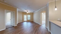 Located at 1930 Devonwood Dr. in Wesley Chapel, FL, this well-appointed 2-bedroom, 2-bathroom single-story home offers a comfortable and functional layout throughout. The open-concept living room features rich hardwood-style flooring, crown molding, and a ceiling fan with light fixture, with direct access to the outdoors through a glass-paned door that invites natural light into the space. The kitchen is equipped with warm wood cabinetry, black appliances including a refrigerator, range, and over-the-range microwave, light tile flooring, and a peninsula breakfast bar accented by pendant lighting overhead — ideal for casual dining or entertaining. The primary bedroom is generously sized, carpeted for comfort, and is served by an en-suite bathroom featuring a walk-in shower, wood-toned vanity, and tile flooring. A spacious walk-in closet with wire shelving provides ample storage. The second bedroom is also carpeted and bright, with multiple windows and a ceiling fan. The second bathroom includes a tub-shower combo, single-sink vanity with a large mirror, and a window for natural ventilation. Neutral warm-beige tones throughout the home create a cohesive and inviting ambiance.