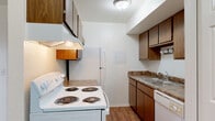 This single-floor unit offers a practical and straightforward layout designed for comfortable everyday living. The kitchen is efficiently arranged with dark wood cabinetry, granite-style laminate countertops, and a full suite of white appliances including a coil-burner electric range, refrigerator, and dishwasher. An overhead range hood, ample upper and lower cabinet storage, and a double-basin sink complete the space, with wood-look flooring running throughout.

The open living area transitions seamlessly from wood-look flooring to plush neutral carpet, creating defined zones within the space. A wall-mounted air conditioning unit and a programmable thermostat ensure year-round climate control, while a large window with vertical blinds allows natural light to fill the room. The front entry door opens directly into this living space, which also connects to the kitchen via an accessible doorway.

The bedroom is generously proportioned, finished with soft carpeting and featuring a window that brings in natural light. A closet with paneled bifold doors provides dedicated storage.

The bathroom is clean and functional, featuring a full tub and shower combination with white tile surround, wood-look flooring, a toilet, and a vanity with matching granite-style countertop. The overall aesthetic throughout the unit is neutral and well-maintained, offering a move-in ready environment.