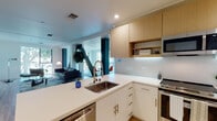 Located at 4770 Telegraph Ave in Oakland's vibrant Temescal neighborhood, this single-floor space showcases a thoughtfully designed modern interior with clean lines and a cohesive contemporary aesthetic throughout. Light hardwood flooring flows seamlessly across the open-concept layout, connecting the kitchen, living, and dining areas into one inviting, well-lit environment.

The kitchen is a standout feature, equipped with stainless steel appliances including a GE range and over-the-range microwave, a deep undermount sink on a peninsula with white quartz countertops, and a striking combination of white lower cabinets and warm natural wood upper cabinetry. A white penny-tile backsplash adds texture and visual interest.

The living and dining areas are generously proportioned, bathed in natural light from large windows that frame views of surrounding greenery. A bold diagonal architectural column serves as a dramatic focal point, lending an industrial-modern character to the space. The dining area accommodates a full table setting, while the living room offers ample room for comfortable seating arrangements.

The bedroom is a serene retreat, featuring a large window with leafy outdoor views and warm hardwood flooring. A light-filled hallway connects the private rooms, accented by colorful wall art. The bathroom is finished with large-format tile flooring, a floating wood vanity with white countertops, and a generous walk-in shower area.