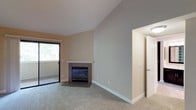 This single-floor residence offers a thoughtfully designed layout with a welcoming open-concept living area at its core. The spacious living room draws the eye upward with vaulted ceilings that lend an airy, expansive feel to the space. A tile-surround fireplace with a white mantel serves as a natural focal point, while a sliding glass door opens to a private balcony, flooding the room with natural light and providing views of surrounding greenery. Neutral-toned carpet throughout the living and bedroom areas adds warmth and comfort underfoot.

The kitchen is well-appointed with white shaker-style cabinetry, dark countertops, stainless steel appliances including a range, microwave, refrigerator, and dishwasher, and durable wood-look flooring. A skylight above brightens the workspace naturally. A peninsula counter connects the kitchen to the main living area for easy flow and functionality.

The bedrooms are generously sized, each featuring plush carpet, large windows with tree-lined views, and ample closet space, including mirrored sliding closet doors in one room. The bathrooms are clean and functional, with one featuring a wide vanity with dark cabinetry and white countertop, and another offering a full tub-shower combo with built-in shelving for storage.