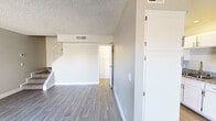 This two-story residence offers a well-organized layout spread evenly across two floors, combining practicality with clean, modern finishes throughout. The main level features a bright living room with neutral gray laminate flooring, textured ceilings, and a sliding glass door that opens directly to a private enclosed patio — an outdoor retreat shaded by a mature tree. The galley-style kitchen is thoughtfully appointed with granite countertops, white cabinetry with brushed gold hardware, a subway tile backsplash, stainless steel appliances, and a double-basin sink. A carpeted staircase with a white railing leads to the upper floor, where both bedrooms are located. The primary bedroom is a generously sized retreat with rich dark hardwood-style flooring and a window that invites natural light and outdoor views. The second bedroom features light laminate flooring and a large window with views of surrounding greenery. Each bathroom features granite-topped vanities with brushed nickel fixtures and clean white finishes. The hallway on the upper level offers additional closet storage and easy access to both bedrooms and bathrooms. Throughout the home, a consistent neutral color palette and modern updates create a cohesive, move-in-ready environment.