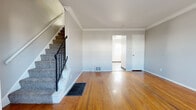 Located at 3556 Greenwich St in Columbus, OH, this two-story home offers a practical and comfortable layout across two floors. The main level features two living areas, with warm-toned hardwood flooring that flows throughout, accented by crown molding that adds a classic architectural touch. Natural light filters in through windows, brightening the open feel of the living spaces. A staircase with a black metal railing connects the floors and serves as a visual focal point on the main level. The kitchen is equipped with gray cabinetry, a modern faucet, and a full-size refrigerator, with wood-look flooring tying it seamlessly to the adjoining areas. The upper floor houses two bedrooms, each finished with plush carpet and windows that allow in natural light. The primary bedroom offers a generous amount of space with a dedicated closet. The full bathroom features a shower-tub combination, a wall-mounted sink, and wood-look flooring, all finished in a clean, all-white palette with a small window for ventilation. Additional closets on both floors provide practical storage throughout the home. The neutral gray wall tones and consistent finishes lend a cohesive, move-in-ready appearance to the entire space.