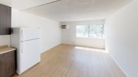 Located at 720 W 27th St in Los Angeles, California, this single-floor unit offers a straightforward and functional layout throughout. The open living area is bright and airy, featuring light wood-style flooring, white walls, and a textured ceiling. A large window fitted with vertical blinds allows generous natural light to fill the space, while a wall-mounted air conditioning unit provides climate control.

The kitchen is efficiently designed with dark wood-grain cabinetry extending to the upper and lower sections, providing ample storage. A stainless steel single-basin sink, a white electric range with coil burners, a built-in range hood, and a microwave complete the cooking area, with light countertops tying the space together.

The bedroom continues the light wood-style flooring and features a sliding-door closet with built-in shelving and a hanging rod, offering practical storage solutions. The room is well-lit by a window that invites natural light.

The bathroom includes wood-style flooring, a dark vanity cabinet with a countertop, a standard toilet, and a bathtub and shower combination enclosed by frosted sliding glass doors with an etched decorative design, adding a classic touch to the room.