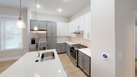 This three-story residence in Charlotte, North Carolina is designed with a clean, modern aesthetic throughout. The ground level includes a spacious two-car garage with an epoxy-coated floor, automatic opener, and a windowed panel door that allows natural light into the space. A hallway with light wood-look flooring connects interior areas, with access to a full bathroom featuring large-format white subway tile, a glass-enclosed walk-in shower, a white vanity with granite-style countertop, and tile flooring.

The main living level showcases a well-equipped kitchen with two-tone gray and white shaker cabinetry, quartz countertops, stainless steel appliances including a gas range and French door refrigerator, a peninsula sink, pendant lighting, and recessed lighting above light hardwood floors.

Upper-level bedrooms are finished with plush carpeting and ceiling fans. The primary bedroom features a large window with exterior views, while the walk-in closet provides built-in shelving, double hanging rods, and a built-in dresser. A secondary full bathroom includes a soaking tub with subway tile surround, a curved shower rod, and tile flooring. Neutral wall tones and consistent trim details contribute to a cohesive, move-in-ready atmosphere throughout all three floors.