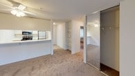 This 2-bedroom, 2-bathroom single-floor unit features a practical, efficient layout designed to maximize usable living space. The kitchen is equipped with stainless steel appliances, including a refrigerator and range, complemented by light-toned countertops and white cabinetry. A pass-through counter connects the kitchen to the main living area, creating an open, communicative flow between spaces. Adjacent to the kitchen, a dedicated laundry or utility alcove provides added convenience.

The living area is finished with wall-to-wall carpeting and neutral wall tones, contributing to a clean, understated ambiance. Built-in open shelving offers practical storage, while a mirrored sliding closet adds depth and functionality. A ceiling fan with integrated lighting serves the secondary bedroom, which also features baseboard heating and a window with leafy outdoor views. The primary bedroom similarly benefits from natural light and baseboard heating.

Both bathrooms are finished with tile flooring and feature tub-shower combinations enclosed by sliding glass doors. Each bathroom includes a window for natural ventilation. One bathroom features a speckled quartz-style countertop vanity, while both maintain a clean, bright aesthetic throughout.