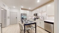 This well-appointed single-floor residence offers a thoughtfully designed layout that balances style and functionality. The kitchen serves as a centerpiece of the home, showcasing crisp white shaker cabinetry extending to the ceiling, a classic white subway tile backsplash, and a full suite of stainless steel appliances including a french door refrigerator, range, microwave, and dishwasher. Light wood-tone flooring flows throughout, lending a clean, contemporary aesthetic. The kitchen opens directly to a dedicated dining area, creating an effortless space for everyday meals or entertaining.

The living room is bright and welcoming, featuring a ceiling fan, light-toned walls, and a glass-paned door that leads to a private balcony overlooking greenery, allowing natural light to fill the space.

Two bedrooms offer comfortable retreats, with carpeted flooring and windows dressed with blinds and sheer curtains for adjustable light and privacy. The bathroom features a white vanity with ample counter space, a well-sized mirror, and clean, neutral finishes throughout.

A dedicated in-unit laundry room with a full-size washer and dryer adds a practical convenience. Overall, the unit presents a modern, cohesive design with a light and airy ambiance suitable for comfortable everyday living.
