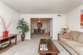 Located at 464 N Oakley Dr in Columbus, Georgia, this single-story residential unit offers a well-organized and functional layout designed for comfortable everyday living. The living room features plush carpeting, ample natural light from a large window, and a warm, welcoming ambiance. A central hallway connects the main living areas to the private spaces, providing a clear and practical flow throughout the unit. The kitchen is outfitted with rich, dark wood cabinetry that extends to the upper walls, light-toned countertops, a double sink, a dishwasher, and a full-size refrigerator. A pass-through breakfast bar connects the kitchen to the adjacent dining area, which comfortably accommodates a full dining table and chairs. The bedroom is generously sized with carpeted flooring, a large window, and access to a spacious walk-in closet featuring dual hanging rods and shelving on both sides. Two bathrooms serve the unit — one featuring a wide vanity with an extended countertop and large mirror, and a second more compact bathroom with a shower-tub combination. Textured ceilings are found throughout, and the neutral color palette across all rooms creates a cohesive and understated aesthetic throughout the space.
