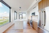 Located at 600 Howard Rd SE in Washington, DC, this thoughtfully designed one-bedroom, two-bathroom residence offers a clean, contemporary aesthetic throughout. Light-toned hardwood flooring flows seamlessly across the open-plan layout, complemented by crisp white walls and modern finishes. The combined kitchen and dining area serves as the heart of the home, anchored by a large waterfall-edge island with an integrated sink, stainless steel appliances, warm wood cabinetry, white upper cabinets, and a tile backsplash — all illuminated by pendant lighting and floor-to-ceiling windows that flood the space with natural light. The living room extends to a private patio through glass-paned doors, offering panoramic views of the Anacostia River and the broader DC skyline. The spacious primary bedroom features corner windows and direct patio access, further enhancing the elevated views. A versatile den provides flexibility for a home office or guest space. Both bathrooms are finished with large-format tile flooring and warm wood vanities, with the second bath featuring a soaking tub and stone-tiled surround. Four closets ensure ample storage throughout. The hallways are bright and efficiently designed, maintaining the residence's modern, uncluttered feel.
