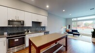 Located at 100 Moffett Blvd in Mountain View, California, this single-floor residence offers a thoughtfully designed layout with modern finishes throughout. The open-concept kitchen and living area serves as the heart of the home, featuring warm hardwood flooring that flows seamlessly across the space. The kitchen is outfitted with full-height white cabinetry, a striking blue-gray subway tile backsplash, stainless steel appliances including a gas range, microwave, refrigerator, and dishwasher, complemented by dark quartz countertops. A central kitchen island with a neutral countertop provides additional prep and storage space. The living area benefits from expansive floor-to-ceiling windows and a glass door that opens to the outdoors, filling the space with abundant natural light and offering views of the surrounding streetscape and greenery. The bedroom is a calm retreat with hardwood flooring, neutral gray walls, and a well-sized window that invites natural light. The bathroom is finished with a clean, contemporary aesthetic, showcasing white cabinetry with dark quartz counters, an oversized LED-backlit mirror, and a soaking tub with a marble-style tiled surround. Throughout the residence, recessed lighting and a neutral color palette create a bright, cohesive ambiance.