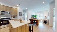 This well-appointed single-floor residence showcases a contemporary design with a cohesive warm aesthetic carried throughout every room. The open-concept layout seamlessly connects the kitchen, dining, and living areas, creating an inviting and functional central living space. Light hardwood flooring flows throughout, complementing the crisp white walls and recessed lighting overhead.

The kitchen is a standout feature, outfitted with flat-front wood-tone cabinetry extending to the ceiling, white quartz countertops, a tiled backsplash, and a full suite of stainless steel appliances including a refrigerator, range, and microwave. A central island with bar seating provides additional prep space and casual dining options. The adjacent dining area and living room benefit from an abundance of natural light, with French doors opening onto a private balcony.

The primary bedroom is a serene retreat, offering generous proportions, large windows with roller shades, and a well-proportioned en-suite bathroom featuring a dual-sink vanity with wood cabinetry, a walk-in glass shower, and hardwood-style flooring. A second bedroom includes a closet with sliding doors and easy access to a full hall bathroom complete with a soaking tub and shower combination. The overall ambiance is bright, clean, and modern throughout.