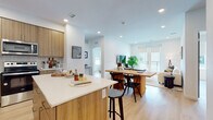 This well-appointed single-floor residence showcases a contemporary design with a cohesive warm aesthetic carried throughout every room. The open-concept layout seamlessly connects the kitchen, dining, and living areas, creating an inviting and functional central living space. Light hardwood flooring flows throughout, complementing the crisp white walls and recessed lighting overhead.

The kitchen is a standout feature, outfitted with flat-front wood-tone cabinetry extending to the ceiling, white quartz countertops, a tiled backsplash, and a full suite of stainless steel appliances including a refrigerator, range, and microwave. A central island with bar seating provides additional prep space and casual dining options. The adjacent dining area and living room benefit from an abundance of natural light, with French doors opening onto a private balcony.

The primary bedroom is a serene retreat, offering generous proportions, large windows with roller shades, and a well-proportioned en-suite bathroom featuring a dual-sink vanity with wood cabinetry, a walk-in glass shower, and hardwood-style flooring. A second bedroom includes a closet with sliding doors and easy access to a full hall bathroom complete with a soaking tub and shower combination. The overall ambiance is bright, clean, and modern throughout.