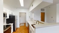 This single-floor residence offers a clean, functional layout designed for comfortable everyday living. The galley-style kitchen is a standout feature, showcasing white shaker cabinetry, light quartz countertops, and a full suite of stainless steel appliances including a refrigerator, electric range, microwave, and dishwasher. Warm hardwood flooring runs throughout the kitchen, adding a natural contrast to the bright white finishes. A skylight overhead floods the space with natural light, enhancing the open, airy feel.

The living areas are finished with plush wall-to-wall carpeting and feature high ceilings that contribute to a spacious atmosphere. Multiple windows dressed with horizontal blinds allow generous natural light and outdoor views, while ceiling fans provide added comfort. The primary bedroom continues this theme with carpet flooring, a ceiling fan, and a window overlooking the outdoors.

The bathroom is well-equipped with a tub-shower combination, a large vanity mirror, white cabinetry, and quartz countertops, maintaining the cohesive design language found throughout the home. A dedicated in-unit laundry room with a full-size washer and dryer adds exceptional practicality. The overall aesthetic is bright, neutral, and move-in ready.