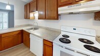 Located at 1150 Vine St in Liverpool, NY, this single-floor unit offers a well-organized layout designed for comfortable everyday living. The main living area is finished with light-toned luxury vinyl plank flooring that lends a clean, modern aesthetic. Large sliding glass doors dressed with vertical blinds allow natural light to flow in and provide access to an outdoor area. A wall-mounted air conditioning unit and baseboard heating ensure year-round climate control throughout the space.

The kitchen is thoughtfully equipped with warm wood cabinetry, light marbled countertops, a stainless steel sink, and white appliances including an electric range and dishwasher. Light wood-style flooring ties the kitchen neatly into the overall design.

The bedrooms feature wall-to-wall carpeting in a neutral tone, providing warmth underfoot. Each room benefits from natural light through windows with blinds, and at least one bedroom includes a closet with bifold doors. Soft gray walls throughout create a calm, cohesive atmosphere.

The bathroom is a standout space, showcasing large-format dark gray marble-look tile surrounding a full soaking tub and shower, complemented by matte black fixtures. Light wood flooring, a white vanity, and clean white walls complete the refined look of this well-appointed room.