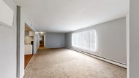 This 2-bedroom, 1-bathroom unit in Detroit, MI is designed with a functional single-floor layout that makes efficient use of its space. The living room serves as the centerpiece of the unit, featuring plush wall-to-wall carpeting, soft gray walls, and a large window fitted with vertical blinds that flood the room with natural light. A baseboard heating system runs along the exterior wall, ensuring comfortable warmth throughout the colder months.

The galley-style kitchen is outfitted with white cabinetry, dark laminate countertops, a stainless steel sink, and white appliances including a refrigerator and electric range. Warm hardwood-style flooring adds a welcoming contrast to the neutral palette.

Both bedrooms continue the carpeted flooring and gray tones, each benefiting from natural light through large windows with vertical blinds and baseboard heaters. One bedroom features a closet with bifold doors and built-in shelving, while the other includes a reach-in closet for additional storage.

The full bathroom is clean and straightforward, featuring tile flooring, a white vanity with storage, a toilet, and a tub-shower combination with white tile surround. The overall layout, as visible in the floor plan, flows logically from the living area through to the private bedrooms and shared bathroom.