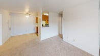 This 2-bedroom, 2-bathroom residence is laid out across a single floor, offering a practical and comfortable living arrangement. The open living area features plush wall-to-wall carpeting and a ceiling fan with integrated lighting, creating a bright and airy atmosphere. A sliding glass door leads to a private balcony, allowing natural light to pour in and providing a pleasant outdoor connection. The kitchen is designed in a galley style, featuring warm wood cabinetry lining both walls, white appliances including a range and refrigerator, a double-basin sink, and durable vinyl flooring — offering ample counter and storage space for everyday cooking. A pass-through opening connects the kitchen to the main living area, enhancing the sense of openness. Both bedrooms are carpeted and include ceiling fans with natural light provided by windows with blinds. The primary bedroom features a walk-in closet and direct access to an en-suite bathroom. Each bathroom is equipped with a vanity with a wide mirror, a single sink with wood cabinetry below, and a shower-tub combination. The layout is efficient and well-organized, making the most of the available space throughout.