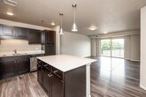 Located at 45 W Jefferson St in Waterloo, Iowa, this 2-bedroom, 1-bathroom residence offers a thoughtfully designed single-floor layout with modern finishes throughout. The open-concept kitchen and living area serves as the heart of the home, anchored by a large center island with a light quartz countertop and dark cabinetry. The kitchen is fully equipped with stainless steel appliances, including a refrigerator, range, and microwave, and is accented by stylish pendant lighting. The living room flows seamlessly from the kitchen and features wood-style plank flooring, a textured ceiling, and a full-width sliding glass door that opens to a private balcony with scenic outdoor views, flooding the space with natural light. Both bedrooms are comfortably sized, featuring the same wood-style flooring, neutral walls, and ample closet space with double-door closets. The space includes a total of four closets, providing generous storage throughout. The bathroom is well-appointed with dark cabinetry, a white countertop vanity, a large mirror, and wood-style flooring that ties in with the rest of the home. A dedicated utility room and hallway complete the layout, contributing to a functional and cohesive living environment.