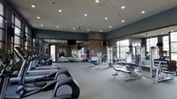 This fitness center is a thoughtfully designed, single-floor facility built to accommodate a comprehensive workout experience. The space is generously sized, providing ample room to move freely between stations without feeling crowded. Cardio equipment, including ellipticals and rowing machines, lines the floor alongside a variety of strength training machines and adjustable benches, catering to a full range of fitness routines. Exercise balls and additional accessories are neatly arranged, adding versatility to the workout options available. Floor-to-ceiling mirrors span the walls, enhancing the sense of openness while allowing users to monitor their form during exercise. Recessed lighting and ceiling fans ensure the space remains well-lit and comfortably ventilated throughout. Large windows along one side of the room invite abundant natural light and offer views of the surrounding exterior, creating an energizing atmosphere. The neutral-toned carpet and dark accent walls give the space a clean, modern aesthetic. Mounted televisions provide entertainment during workouts, rounding out the practical and inviting design of this well-appointed fitness facility.