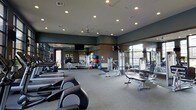 This fitness center is a thoughtfully designed, single-floor facility built to accommodate a comprehensive workout experience. The space is generously sized, providing ample room to move freely between stations without feeling crowded. Cardio equipment, including ellipticals and rowing machines, lines the floor alongside a variety of strength training machines and adjustable benches, catering to a full range of fitness routines. Exercise balls and additional accessories are neatly arranged, adding versatility to the workout options available. Floor-to-ceiling mirrors span the walls, enhancing the sense of openness while allowing users to monitor their form during exercise. Recessed lighting and ceiling fans ensure the space remains well-lit and comfortably ventilated throughout. Large windows along one side of the room invite abundant natural light and offer views of the surrounding exterior, creating an energizing atmosphere. The neutral-toned carpet and dark accent walls give the space a clean, modern aesthetic. Mounted televisions provide entertainment during workouts, rounding out the practical and inviting design of this well-appointed fitness facility.