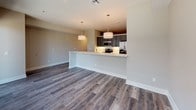 This thoughtfully designed single-floor residence offers a seamless blend of modern finishes and functional living spaces. The open-concept layout connects the kitchen and living area effortlessly, with rich wood-look flooring running throughout the main living spaces. The kitchen is a standout feature, boasting sleek gray cabinetry, quartz countertops, stainless steel appliances including a range, microwave, and refrigerator, a deep double-basin sink, and pendant lighting that adds a contemporary touch. A peninsula counter provides a natural transition into the living area, which is bathed in natural light from large windows and a sliding glass door that opens onto a private balcony overlooking the surrounding neighborhood. The bedroom is finished with plush carpeting, neutral-toned walls, and a ceiling fan, offering a quiet and comfortable retreat. A generous walk-in closet with built-in shelving and hanging rods provides ample storage. The bathroom is finished with large-format tile flooring, a tiled tub-shower combination with a showerhead and curtain rod, a white vanity with quartz countertops and an undermount sink, and a well-lit mirror. Throughout the space, clean lines, neutral tones, and quality finishes create a cohesive and inviting atmosphere.
