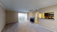 This single-floor residential unit offers a well-planned layout that balances functionality and comfort throughout its living spaces. The main living area is generously proportioned, featuring plush wall-to-wall carpeting, crown molding, and a textured ceiling with track lighting. A standout feature is the tile-surround fireplace, which anchors the room and adds a warm focal point. Sliding glass doors with vertical blinds flood the space with natural light and provide access to an outdoor area. Adjacent to the living room, the kitchen is accessible via a breakfast bar pass-through with dark granite countertops, offering a seamless connection between spaces. The kitchen is equipped with dark cabinetry, a tile backsplash, and stainless steel appliances including a refrigerator, microwave, and range. Wood-look flooring runs through the kitchen and extends into the bathroom, which features a dark-vanity with a granite countertop and a well-lit mirror. The bedrooms are carpeted and include crown molding, ceiling fans with light fixtures, and windows with blinds that allow for natural light and privacy. Throughout the unit, neutral warm-toned walls and consistent finishes create a cohesive and inviting atmosphere.