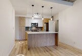 Located in Edmonton's vibrant Oliver neighbourhood, this thoughtfully designed 2-bedroom, 1-bathroom unit offers a modern urban living experience with quality finishes throughout. Light-toned luxury vinyl plank flooring flows seamlessly across the entire space, complemented by exposed concrete accents that lend an industrial-chic character to the aesthetic.

The open-concept kitchen serves as the heart of the unit, featuring a central island with a waterfall-edge countertop, sleek white upper cabinetry paired with warm wood-toned lower cabinets, a tiled backsplash, and stainless steel appliances. Pendant lighting and a track light fixture illuminate the space stylishly.

Both bedrooms are well-proportioned, each featuring sliding barn-style closet doors and distinctive grey accent walls. The primary bedroom is generously sized and benefits from floor-to-ceiling windows that invite abundant natural light and offer views of the surrounding cityscape. The second bedroom also enjoys outdoor views through large windows.

The bathroom is cleanly finished with large-format floor tiles, a soaker tub and shower combination with white subway tile surround accented by a mosaic tile detail, and a wood-toned vanity. A dedicated laundry area accommodates a full stacked washer and dryer unit for added convenience.