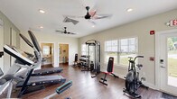 Located at 441 Historic Hwy N in Demorest, Georgia, this fitness facility offers a compact yet fully functional space designed to meet a wide range of exercise needs. The main exercise room is bright and welcoming, with neutral-toned walls, rich hardwood-style flooring, and abundant natural light streaming through multiple windows fitted with slatted blinds. Ceiling fans provide air circulation throughout the workout area, complementing the recessed lighting overhead. The room is outfitted with a comprehensive selection of equipment, including a multi-function cable machine, a full dumbbell rack, an elliptical trainer, a treadmill, a stationary air bike, and a weight bench. Large wall-mounted mirrors on one side of the room enhance the sense of space and allow users to monitor their form during workouts. A frosted-glass interior door adds a clean, modern aesthetic touch. The facility includes two well-maintained bathrooms, each featuring hardwood-style flooring, wall-mounted paper towel dispensers, and stainless steel accessories. One bathroom is equipped with a wall-hung sink, a mirror, and a waste bin, while the other features a standard toilet with a toilet paper holder and a hand dryer. Together, these amenities make this fitness space a practical and polished facility for daily use.