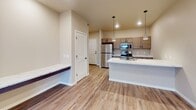 This single-floor, one-bedroom, one-bathroom unit offers a well-designed open-concept layout with consistent wood-look flooring throughout the main living areas. The kitchen serves as a central focal point, featuring a large island with marble-look countertops, a matte black faucet, and generous counter space along the perimeter. Taupe-toned shaker-style cabinetry with black hardware pairs with stainless steel appliances, including a refrigerator, electric range, and built-in microwave. Pendant lighting above the island adds a modern touch, while recessed lighting illuminates the space efficiently.

The open living area extends from the kitchen, offering a spacious and bright environment enhanced by recessed lighting and a sliding glass door that leads to a balcony with outdoor views. A built-in bench near the entryway provides a convenient drop zone.

The bedroom is carpeted for comfort and features a large window that brings in natural light and exterior views. The full bathroom includes a single-sink vanity topped with a marble-look surface, warm wood cabinetry, black hardware accents, and a tub-shower combination, completing this clean and contemporary residence.