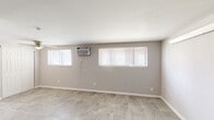 This single-floor unit offers a clean, functional layout with a cohesive design aesthetic carried throughout every room. The flooring is a consistent large-format tile in a neutral stone-like finish, providing a durable and visually unified base across the entire space.

The main living area is generously sized, featuring soft gray walls, white baseboards, and multiple windows fitted with horizontal blinds that allow for natural light control. A wall-mounted air conditioning unit ensures year-round climate comfort. The open, unobstructed layout offers flexibility for a variety of furniture arrangements.

The galley kitchen is efficiently designed with white cabinetry featuring brushed nickel hardware, marble-patterned countertops, a stainless steel double-basin sink, and a white electric range with a ventilation hood above. The clean, bright aesthetic of the kitchen makes practical use of the available space.

The bathroom includes a white vanity with an integrated sink, a large wall mirror with a lighted fixture above, and tiled flooring that complements the rest of the unit. An additional room provides natural light through a window with blinds, offering versatility as a bedroom or flex space. The entry area features a solid white door, completing this straightforward and well-maintained layout.