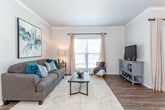 This single-floor residence offers a thoughtfully designed layout with a cohesive aesthetic throughout. The living room serves as a welcoming central space, featuring crown molding, dark hardwood-style flooring, and a large window dressed with neutral curtains that invite natural light. The open layout connects seamlessly to the dining area, which is highlighted by a pendant light fixture, crown molding, and a sliding glass door with vertical blinds that provide additional natural light and outdoor access.

The kitchen is equipped with stainless steel appliances, including a range, microwave, and refrigerator, complemented by dark cabinetry, white subway tile backsplash, and wood-style flooring. The primary bedroom features carpeted flooring, a ceiling fan, large windows with outdoor views, and a walk-in closet. A second carpeted bedroom also includes a ceiling fan and natural light. The bathroom presents dark espresso cabinetry, a wide vanity mirror with overhead lighting, and wood-style flooring. A dedicated in-unit laundry area accommodates a full-size washer and dryer with wire shelving above for storage.
