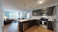 This single-floor residence offers a well-designed open-concept layout that seamlessly connects the kitchen, dining, and living areas. The kitchen is a standout feature, equipped with dark espresso cabinetry, a white quartz countertop peninsula with an integrated sink, and a full suite of stainless steel appliances including a gas range, microwave, dishwasher, and refrigerator. A white subway tile backsplash and three stylish pendant lights add refined detail overhead. Warm hardwood-style flooring extends throughout the main living areas, complementing the soft blue-grey wall tones that create a calm, cohesive ambiance.

The dining area accommodates a full table set and flows naturally into the living room, which is brightened by large windows fitted with blinds. The bedroom is carpeted and comfortably proportioned, featuring natural light from a window and a ceiling fan. It connects to a walk-in closet outfitted with multi-tiered wire shelving for generous storage. The bathroom features light tile flooring, a dark wood vanity with a white countertop, a large mirror, and direct access to the walk-in closet. Throughout, the space maintains a clean, contemporary aesthetic with consistent finishes.